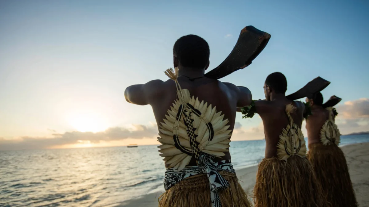 Castaway Island Fiji Meke Performance scaled Fijian dancers performing a traditional Meke dance at Castaway Island Fiji, with the ocean and sunset in the background.